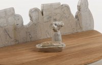 „Brot und Blumen“ (Detail: Griff und Holzdeckel)<br>
aus eigener Tonmischung mit Engobemalerei und Zeichnung unter Zinnglasur.<br>
Die Großfamilie isst zusammen. Der Deckel aus Eiche stellt den Tisch dar. Darauf stehen ein gefüllter Brotkorb mit einem Blumenstrauß in der Vase, der angenehm als Knopf zum Öffnen dient.<br>
Im Topf ziert eine Tischdecke und das Fischgrät-Parkett mit Teppich den Raum für´s Brot.<br>
Maße: l x b x h : 38 x 21,5 x 23,6 cm<br>